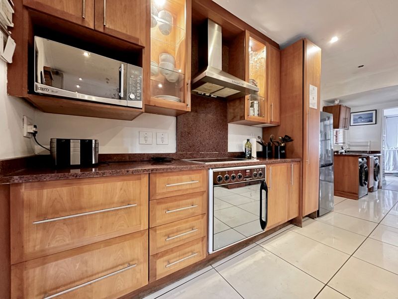 A well-maintained kitchen featuring warm-toned wooden cabinetry, granite countertops, integrated appliances, and polished tile flooring, with an adjacent laundry area visible.