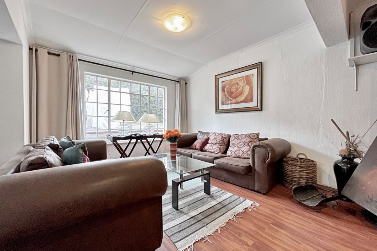 A cozy living room featuring laminate flooring, a grid-pattern window, and a fireplace, offering a comfortable space for relaxation.