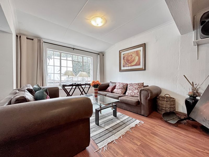 A cozy living room featuring laminate flooring, a grid-pattern window, and a fireplace, offering a comfortable space for relaxation.