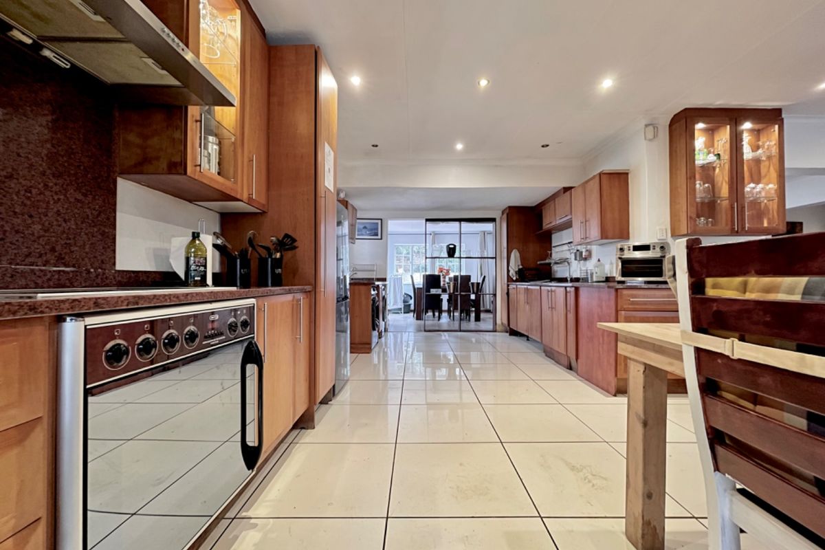 Spacious kitchen featuring extensive wooden cabinetry, granite countertops, integrated appliances, and tiled flooring, leading through to an adjacent dining area.