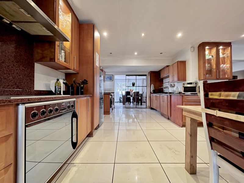 Spacious kitchen featuring extensive wooden cabinetry, granite countertops, integrated appliances, and tiled flooring, leading through to an adjacent dining area.