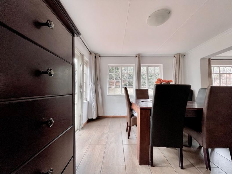 A bright dining room featuring wood-look tiled flooring, multi-pane windows, and direct access to the exterior through a glass panel door.