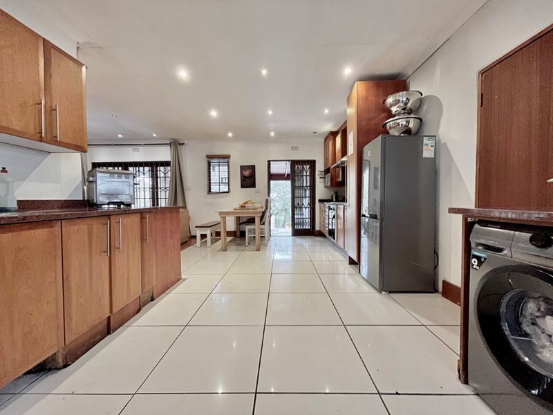 Open-plan kitchen and dining area featuring wood-finish cabinetry, granite countertops, tiled flooring, and recessed lighting, with direct access to the outdoor space.