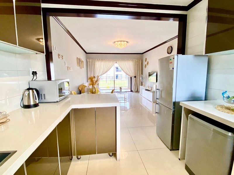 Open-plan kitchen and living area featuring modern cabinetry, quartz countertops, tiled flooring, and direct access to a balcony through sliding doors.