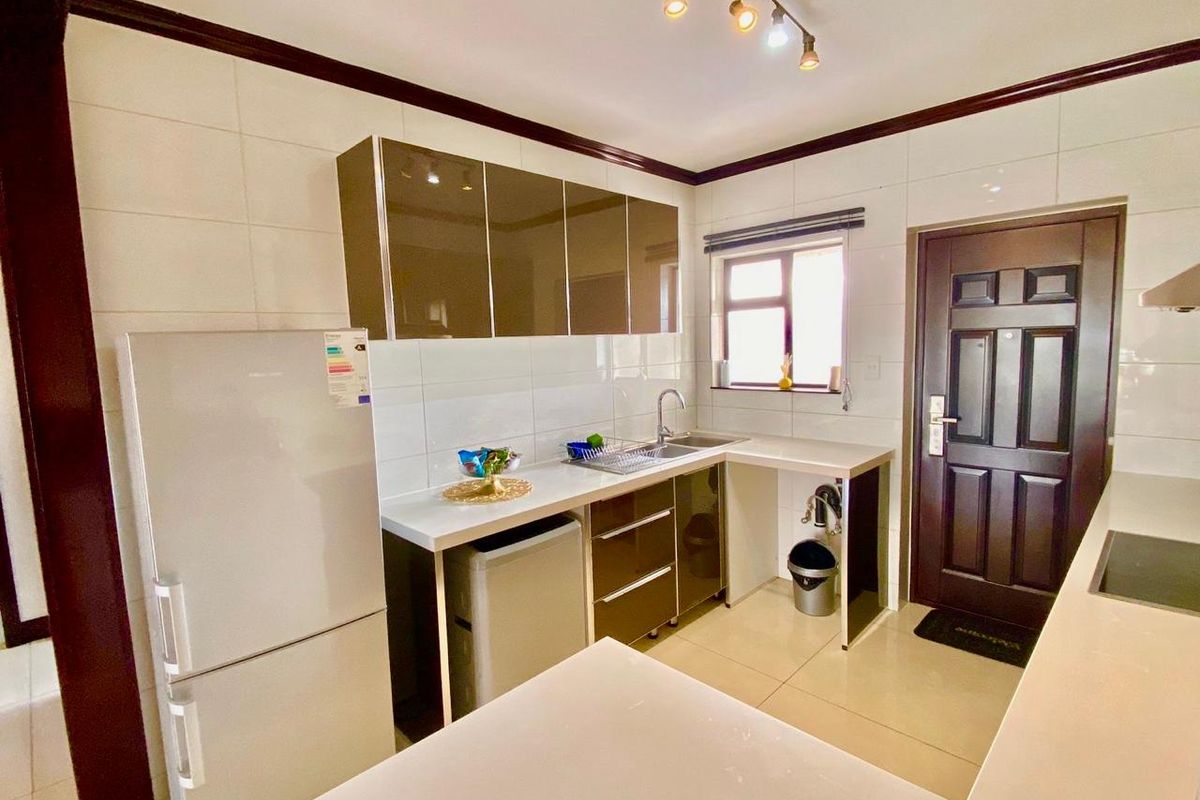 A functional kitchen featuring modern high-gloss cabinetry, tiled walls, and tiled flooring, providing a clean and practical workspace.
