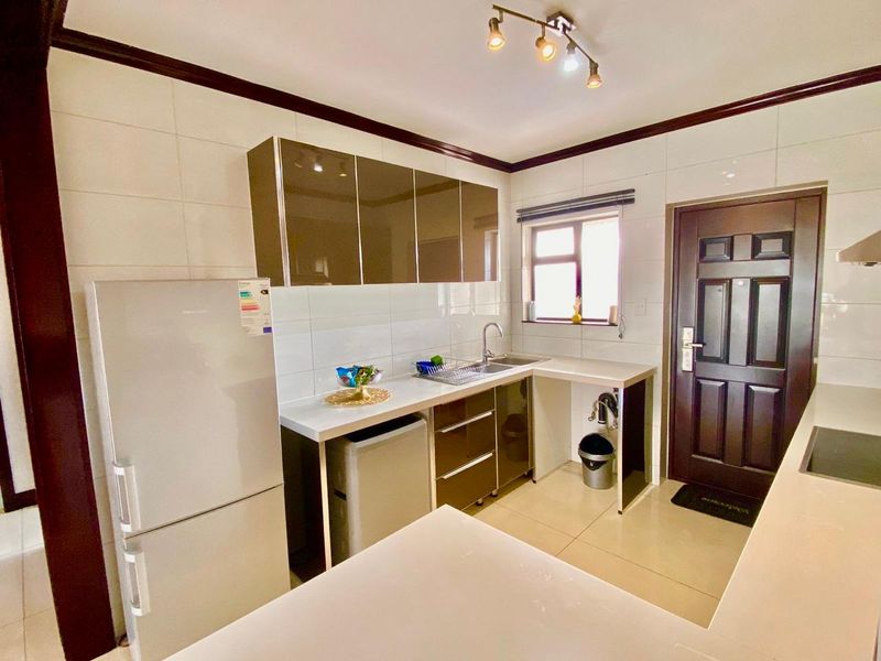 A functional kitchen featuring modern high-gloss cabinetry, tiled walls, and tiled flooring, providing a clean and practical workspace.