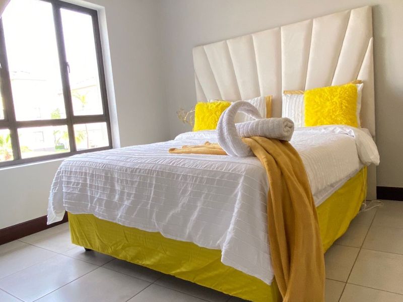 A bright bedroom featuring tiled flooring, crown molding, and a large window allowing for natural light.