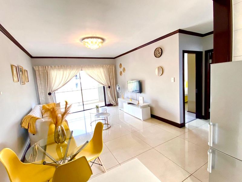 Bright open-plan living and dining area featuring large format floor tiles, crown molding, and a sliding glass door leading to a balcony.