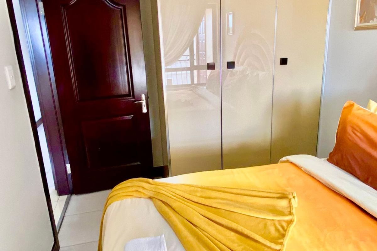 A bedroom featuring a built-in wardrobe with high-gloss finish, tiled flooring, and a dark wood door.