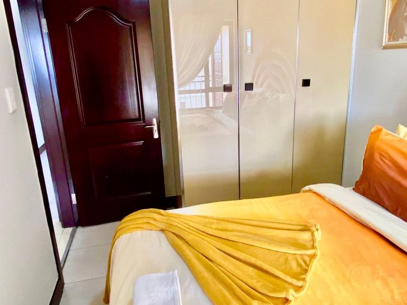 A bedroom featuring a built-in wardrobe with high-gloss finish, tiled flooring, and a dark wood door.