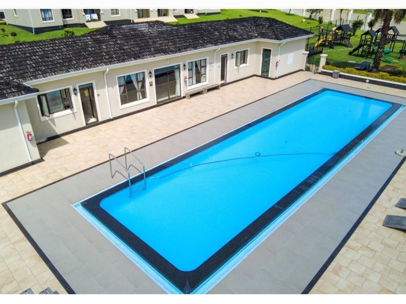 Aerial view of a rectangular swimming pool with a tiled deck, adjacent to a single-story building with a dark tiled roof.