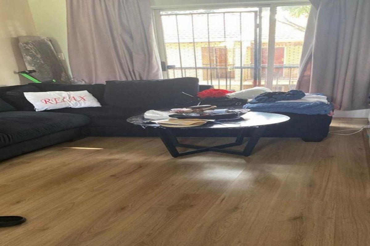 A living room featuring laminate flooring and a sliding glass door with an integrated security gate, providing access to the exterior.