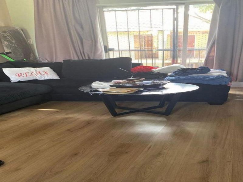 A living room featuring laminate flooring and a sliding glass door with an integrated security gate, providing access to the exterior.