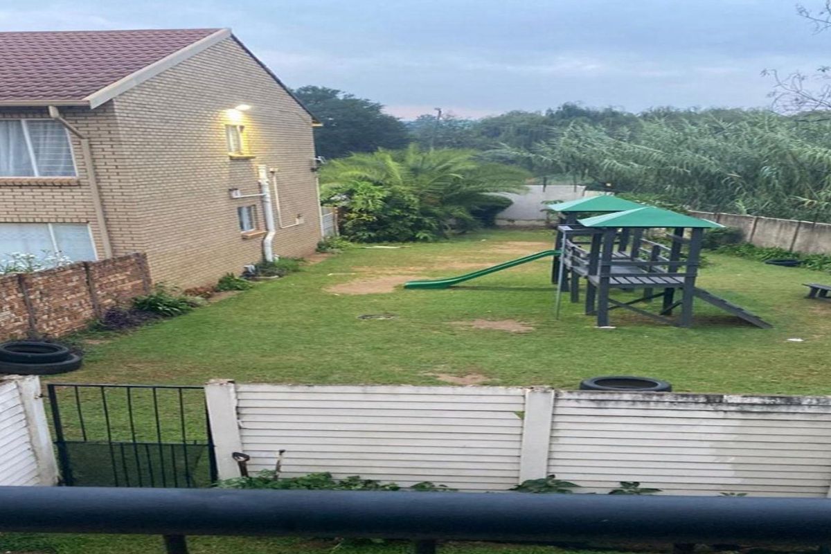 A view of the rear garden area featuring a brick apartment facade, lawn, and perimeter walling.