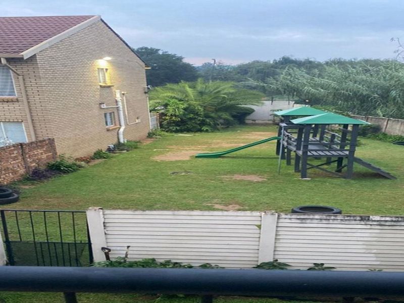 A view of the rear garden area featuring a brick apartment facade, lawn, and perimeter walling.