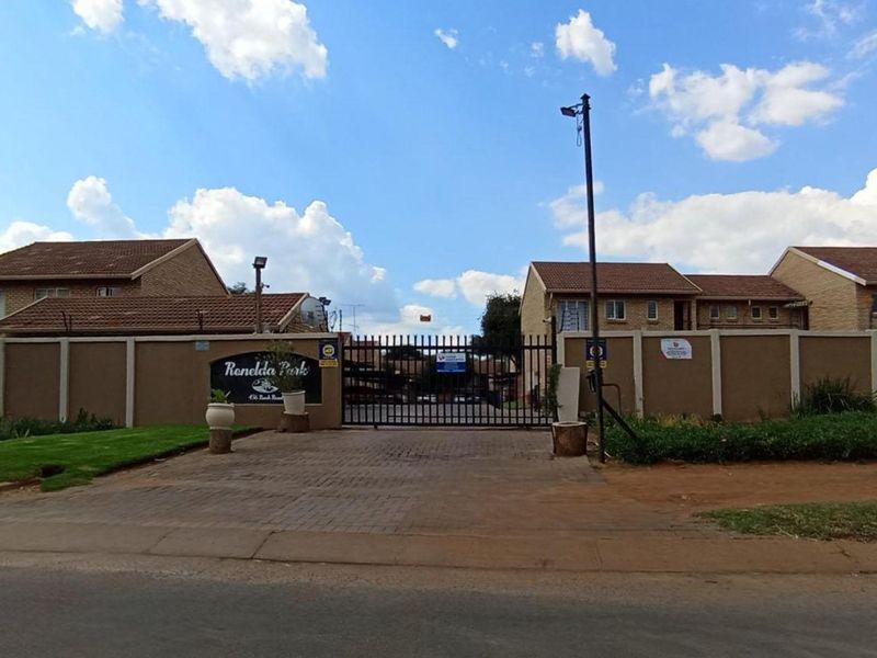 Front entrance view of Ronelda Park apartment complex featuring a secure gated access point, perimeter walling, and paved driveway.