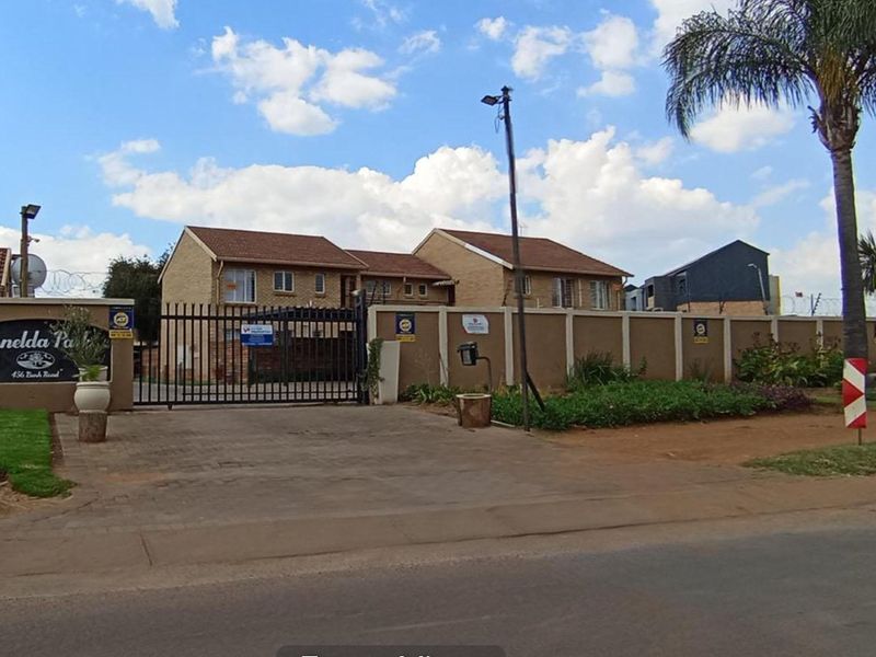 Front exterior view of Ronelda Park apartment complex featuring a secure gated entrance, perimeter wall with electric fencing, and paved driveway access.