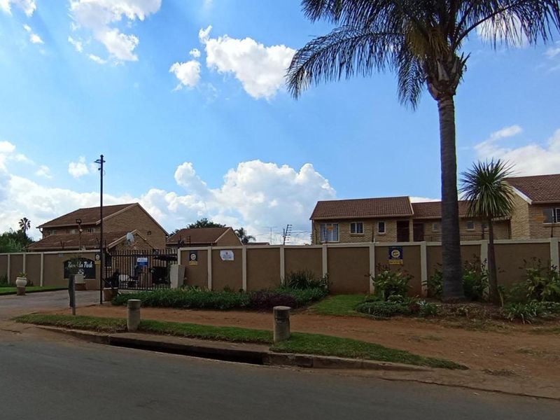 Street view of the apartment complex entrance featuring a secure perimeter wall, gated access, and established landscaping.