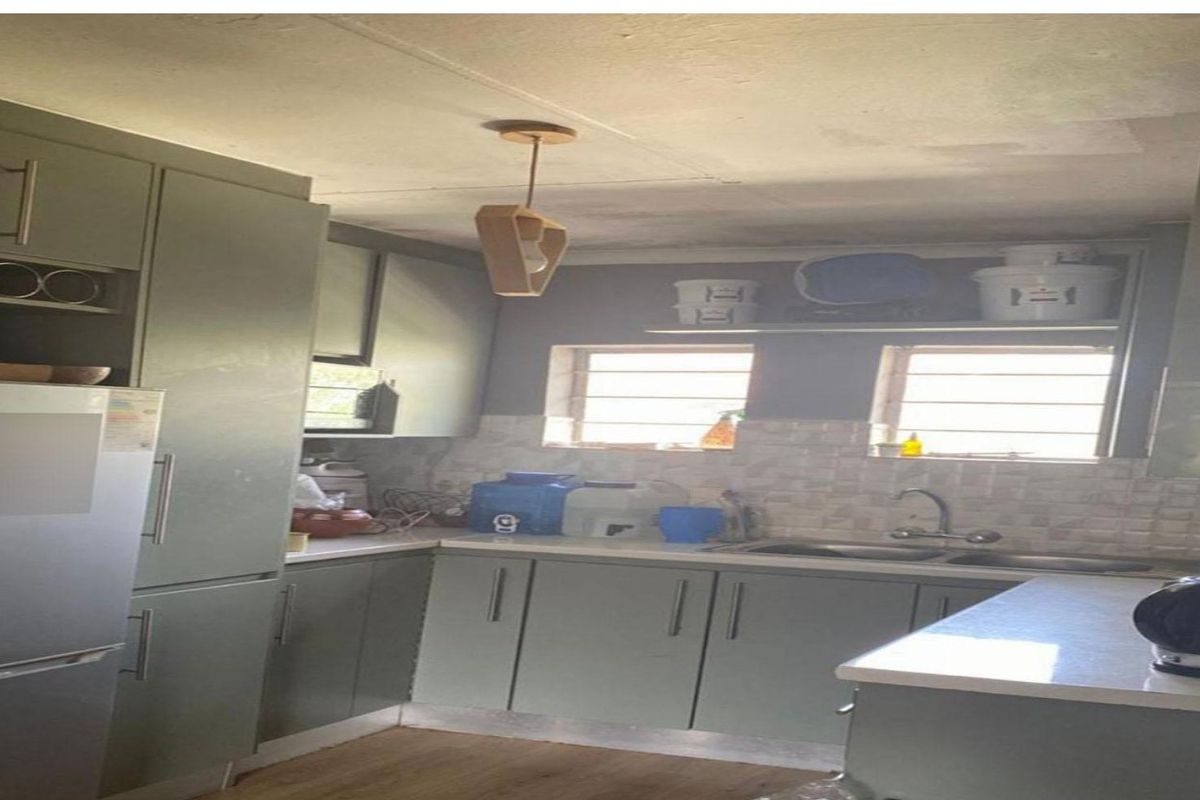 A compact kitchen featuring sage green cabinetry, laminate countertops, a double basin sink, and tiled backsplash, requiring some ceiling maintenance.