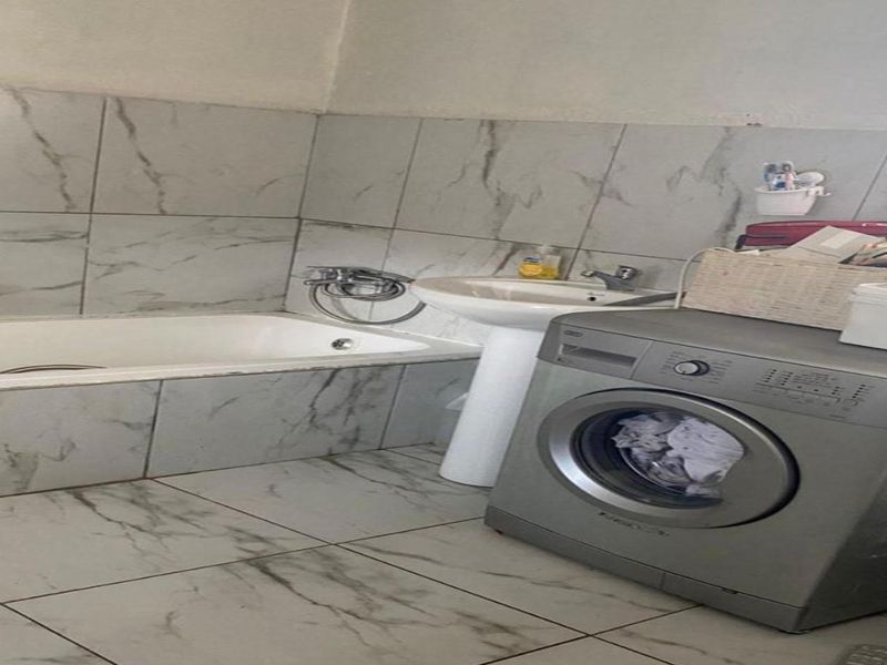 A functional bathroom featuring a bathtub, pedestal basin, and marble-look tiled finishes throughout.