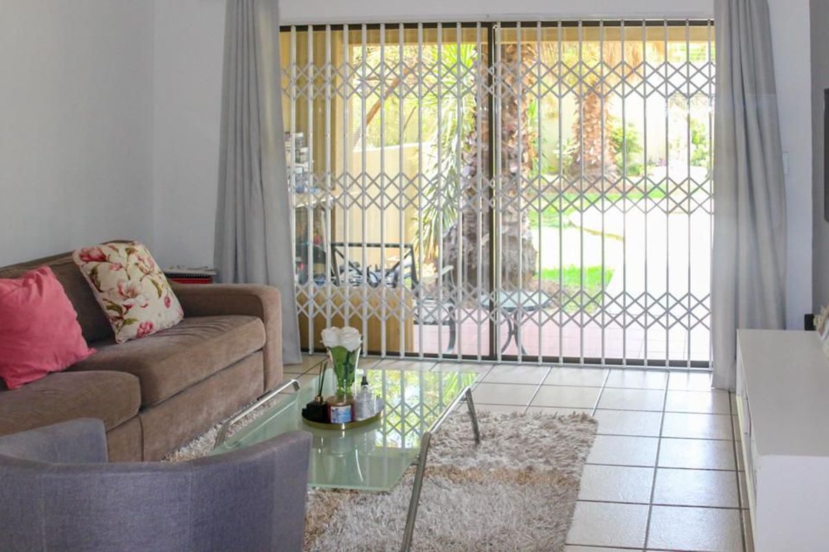 A living room featuring tiled flooring and a sliding glass door with a security gate, providing access to the outdoor area.