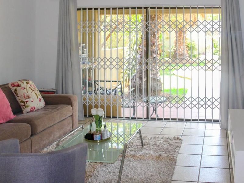 A living room featuring tiled flooring and a sliding glass door with a security gate, providing access to the outdoor area.