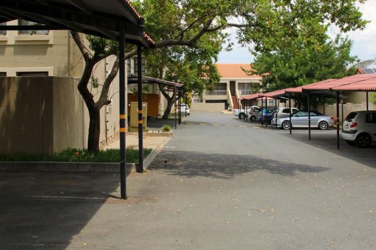 View of the apartment complex parking area featuring covered parking bays and paved driveway access.