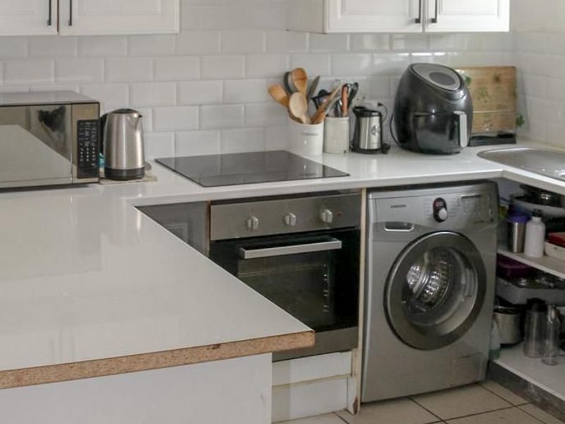 A functional kitchen featuring white cabinetry, subway tile backsplash, built-in oven, electric hob, and integrated laundry appliance with tiled flooring.