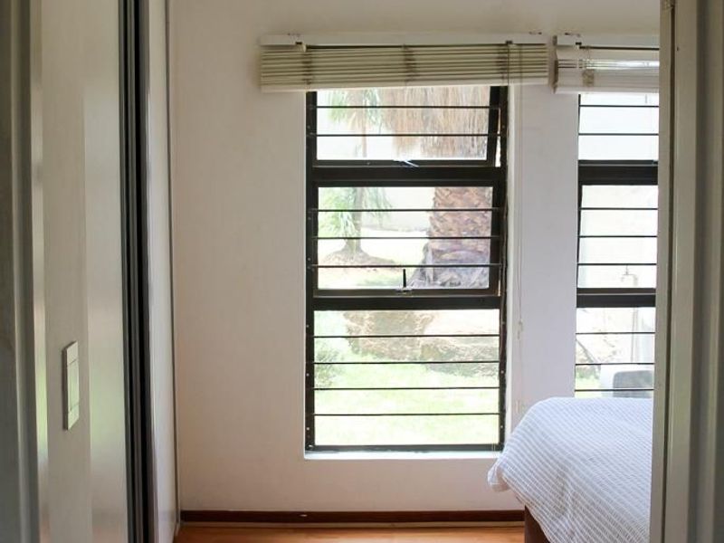 A bedroom featuring laminate flooring, built-in sliding door wardrobes, and windows fitted with security bars and venetian blinds.