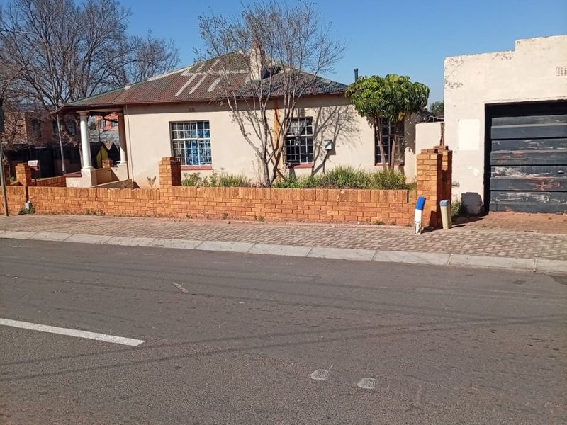 Front view of a single-story house featuring a brick boundary wall, corrugated metal roof, and an attached garage.