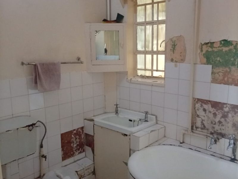A dated bathroom requiring significant renovation, featuring a bathtub, sink, and toilet with visible damage to wall finishes and tiles.