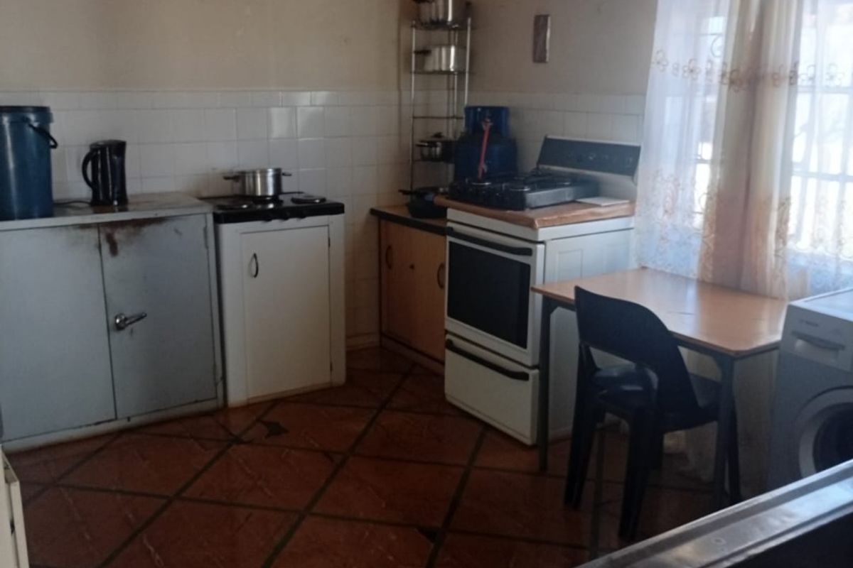 A functional kitchen featuring tiled flooring, a tiled splashback, a freestanding oven, and basic cabinetry, offering potential for modernization and renovation.