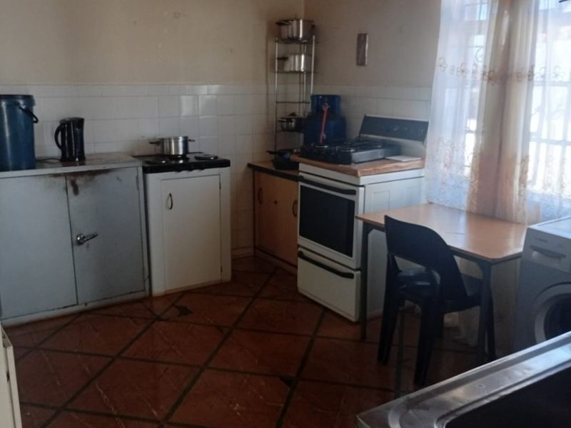 A functional kitchen featuring tiled flooring, a tiled splashback, a freestanding oven, and basic cabinetry, offering potential for modernization and renovation.