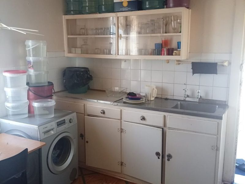 A functional laundry area featuring built-in cabinetry, a stainless steel sink, tiled splashback, and tiled flooring in need of maintenance.