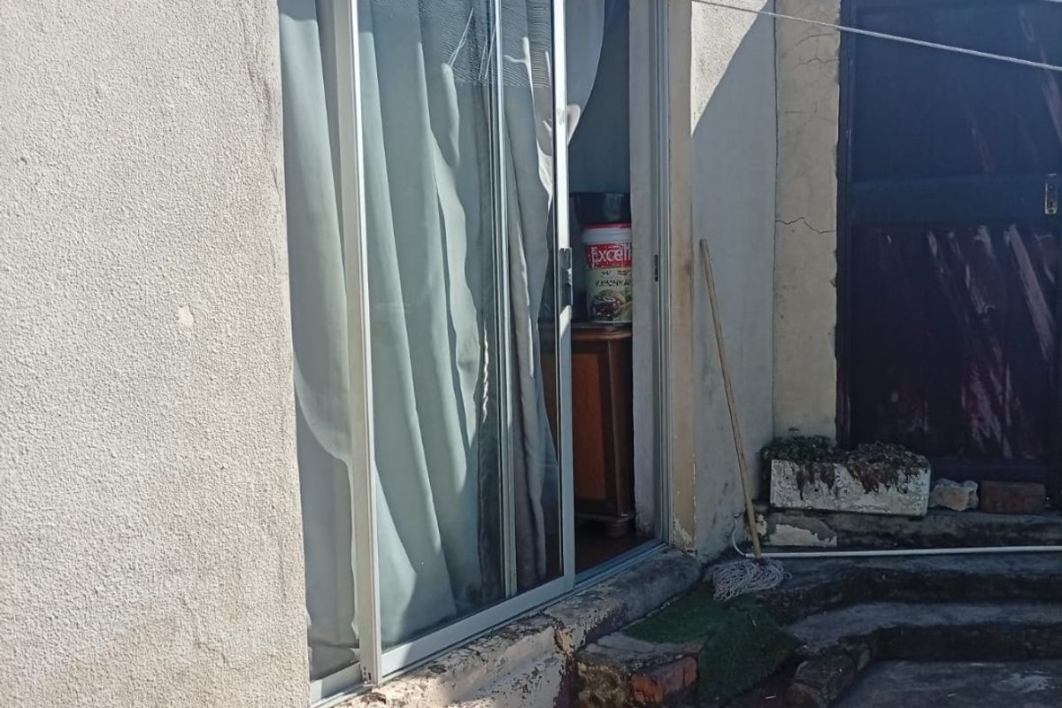 Rear exterior view showing a sliding glass door entrance, concrete patio area, and weathered exterior wall finishes requiring maintenance.