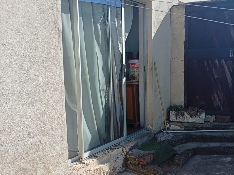 Rear exterior view showing a sliding glass door entrance, concrete patio area, and weathered exterior wall finishes requiring maintenance.