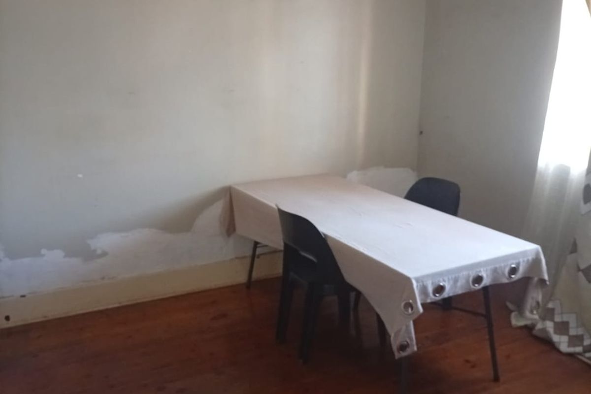 A living area featuring polished timber flooring and walls showing signs of paint deterioration and surface damage.