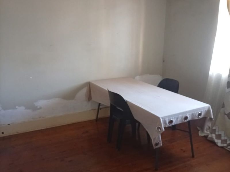 A living area featuring polished timber flooring and walls showing signs of paint deterioration and surface damage.