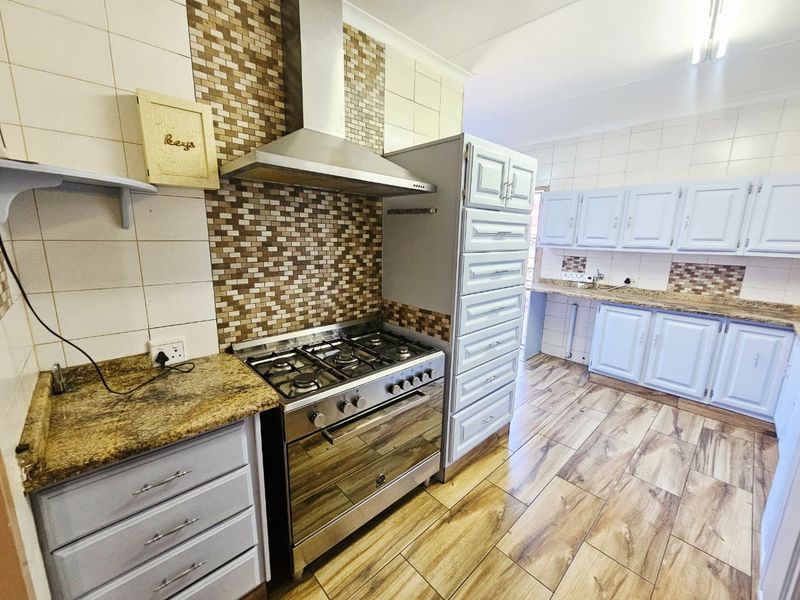A functional kitchen featuring light-toned cabinetry, granite countertops, a gas stove with extractor fan, and durable wood-look floor tiles.
