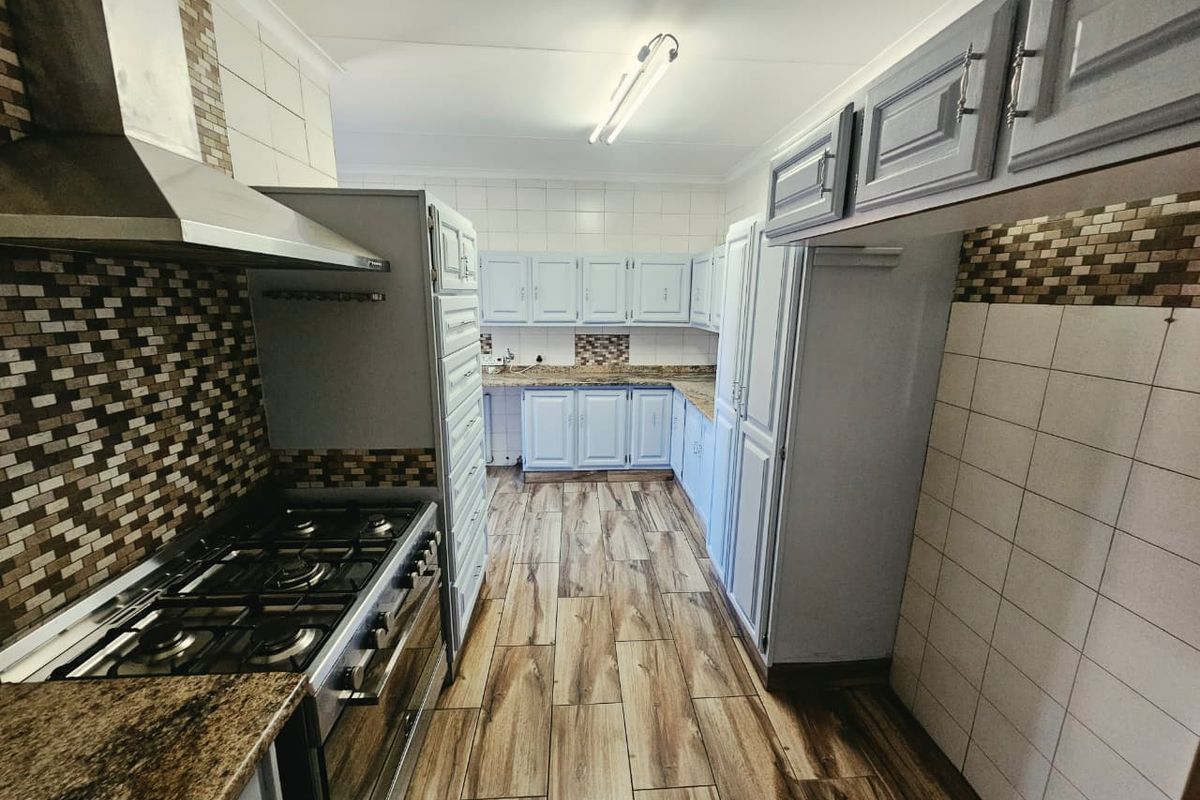 A functional kitchen featuring built-in cabinetry, granite countertops, a gas stove with extractor fan, and modern wood-look floor tiles.
