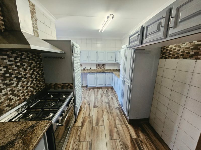 A functional kitchen featuring built-in cabinetry, granite countertops, a gas stove with extractor fan, and modern wood-look floor tiles.