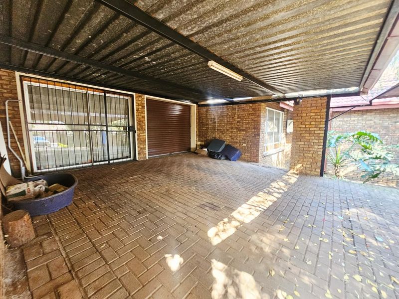A covered outdoor garage or carport area featuring brick walls, paved flooring, and a corrugated metal roof structure.