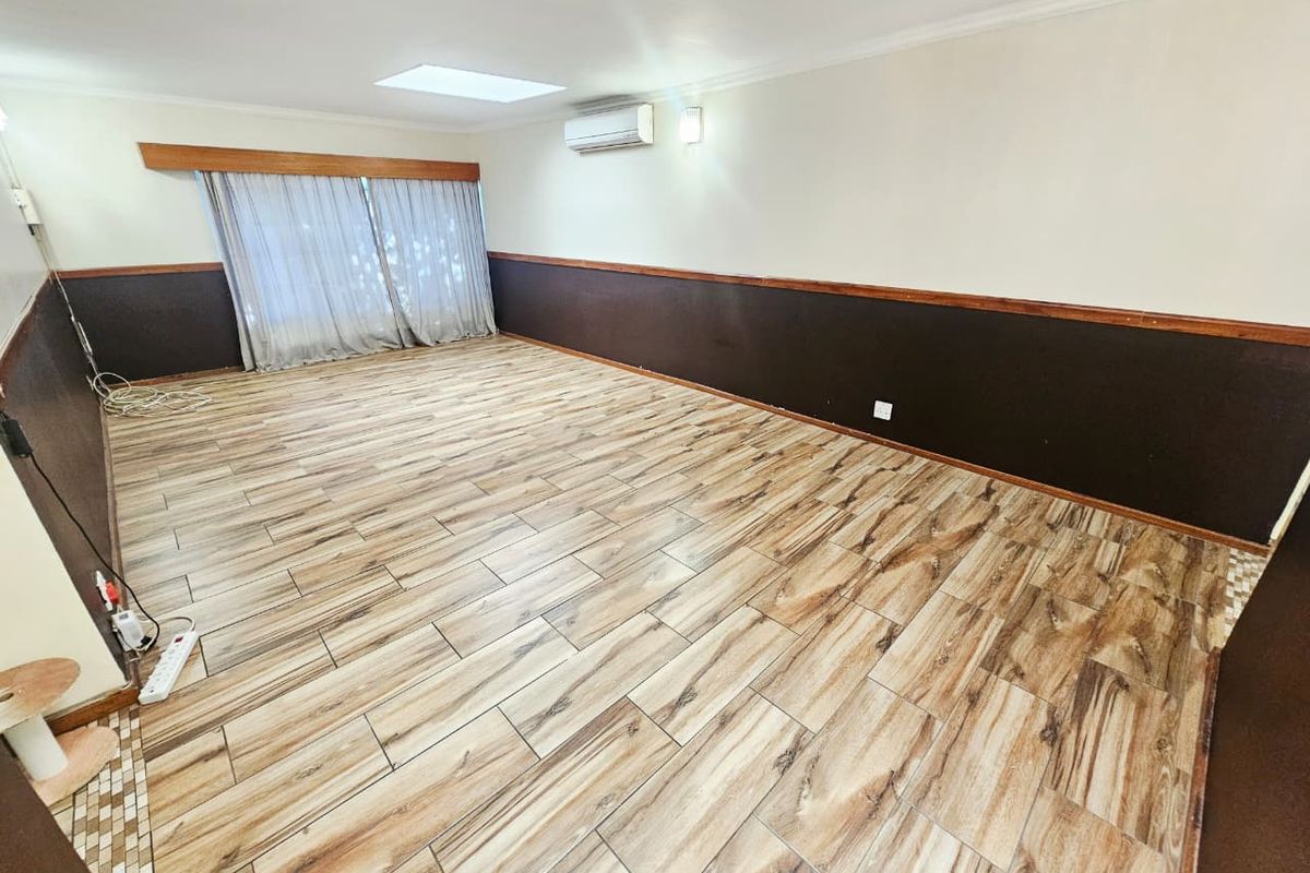 Spacious living area featuring wood-look tile flooring, a wall-mounted air conditioner, and a skylight, providing a neutral canvas for interior design.