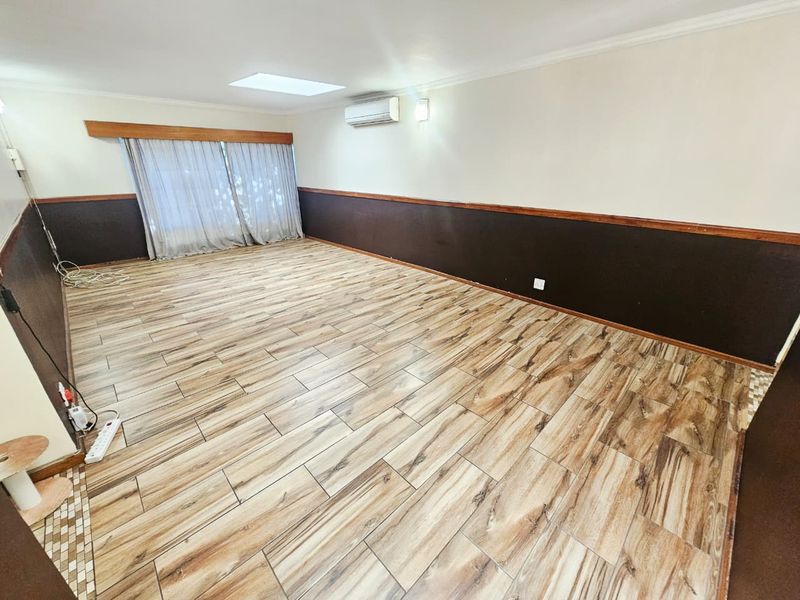 Spacious living area featuring wood-look tile flooring, a wall-mounted air conditioner, and a skylight, providing a neutral canvas for interior design.