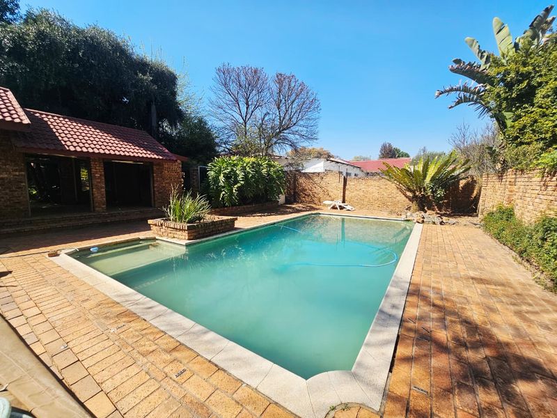 Outdoor pool area featuring a swimming pool, brick paving, and a covered patio structure with a tiled roof.