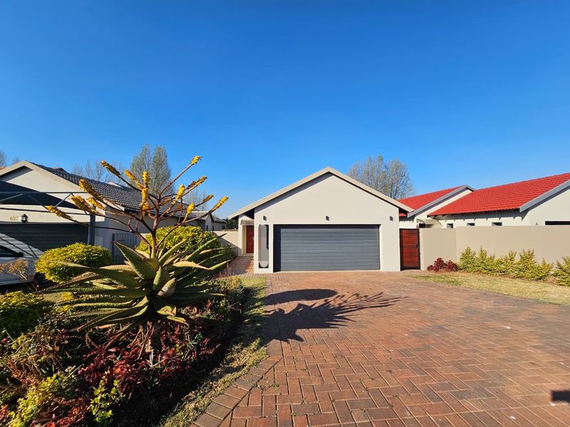 Front elevation of a modern house featuring a paved driveway, a dark grey sectional garage door, and a secure side entrance gate.