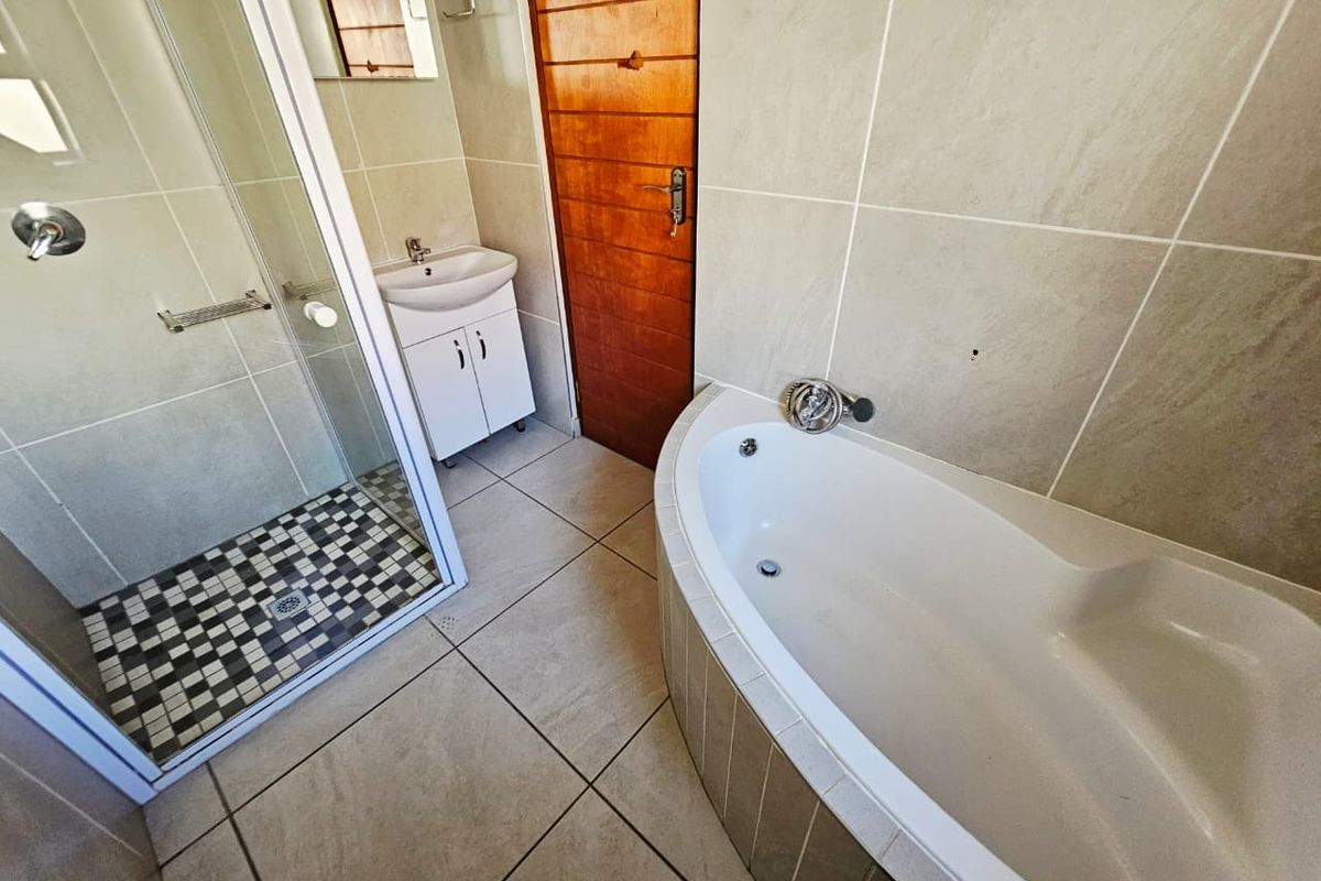 A functional bathroom featuring a corner bathtub, a separate glass-enclosed shower, and a vanity basin with neutral wall and floor tiling.