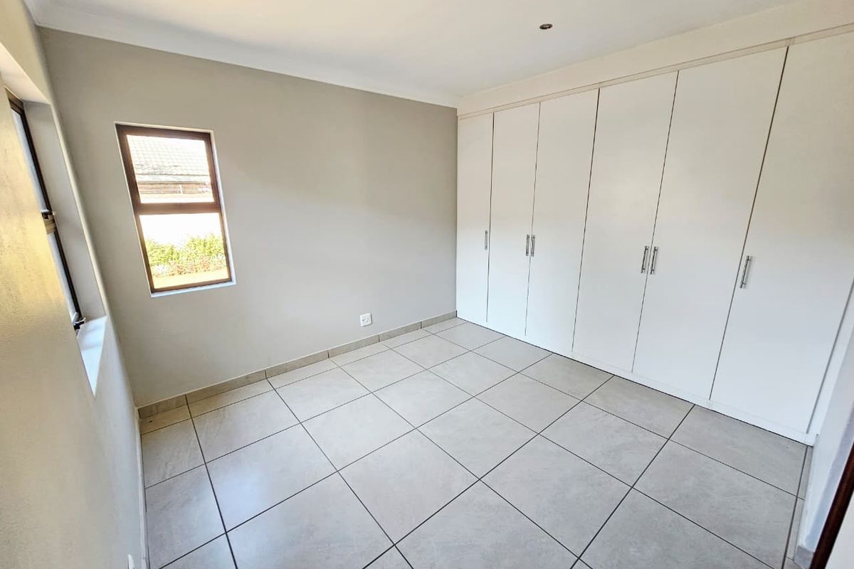 A clean, empty bedroom featuring neutral tiled flooring, recessed downlights, and extensive white built-in cupboards for ample storage.