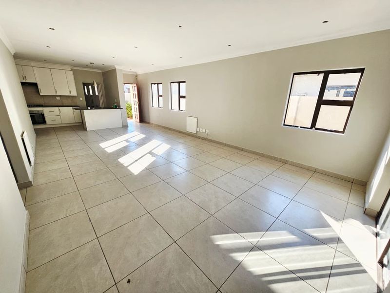 Spacious open-plan living and kitchen area featuring neutral tiled flooring, modern cabinetry, and abundant natural light through multiple windows.