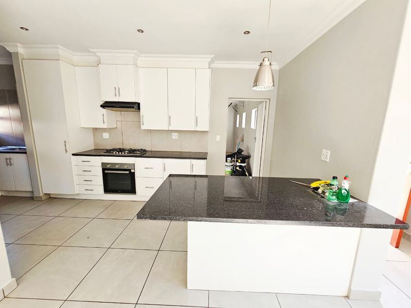 Modern kitchen featuring white cabinetry, granite countertops, a central island, built-in oven, gas hob, and tiled flooring.
